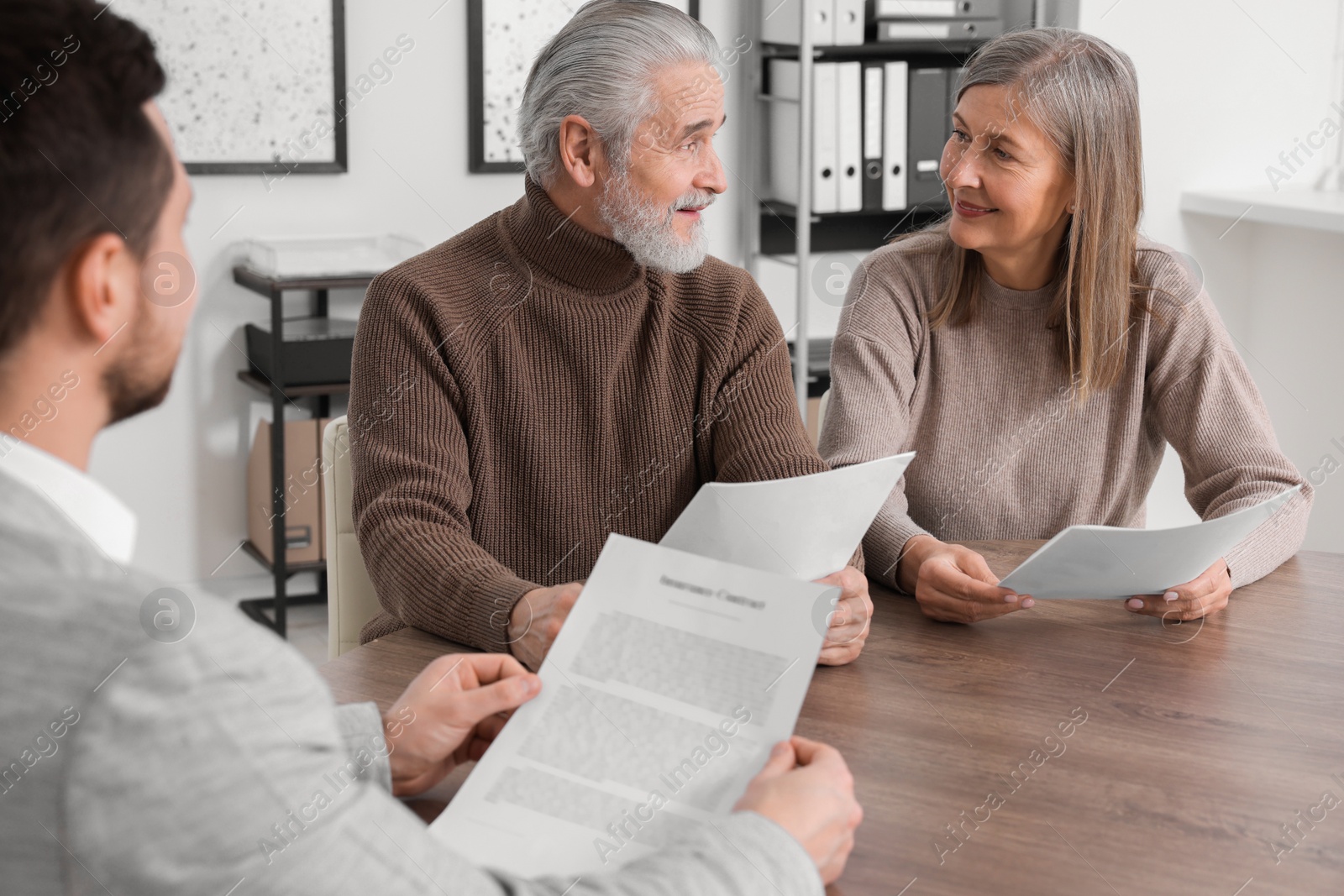 Photo of Elderly couple consulting insurance agent about pension plan at wooden table indoors