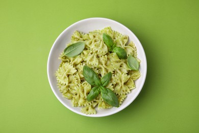 Delicious pasta with pesto sauce and basil on light green background, top view