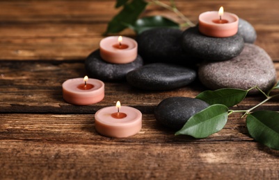 Photo of Composition of spa stones, green leaves and burning candles on wooden table
