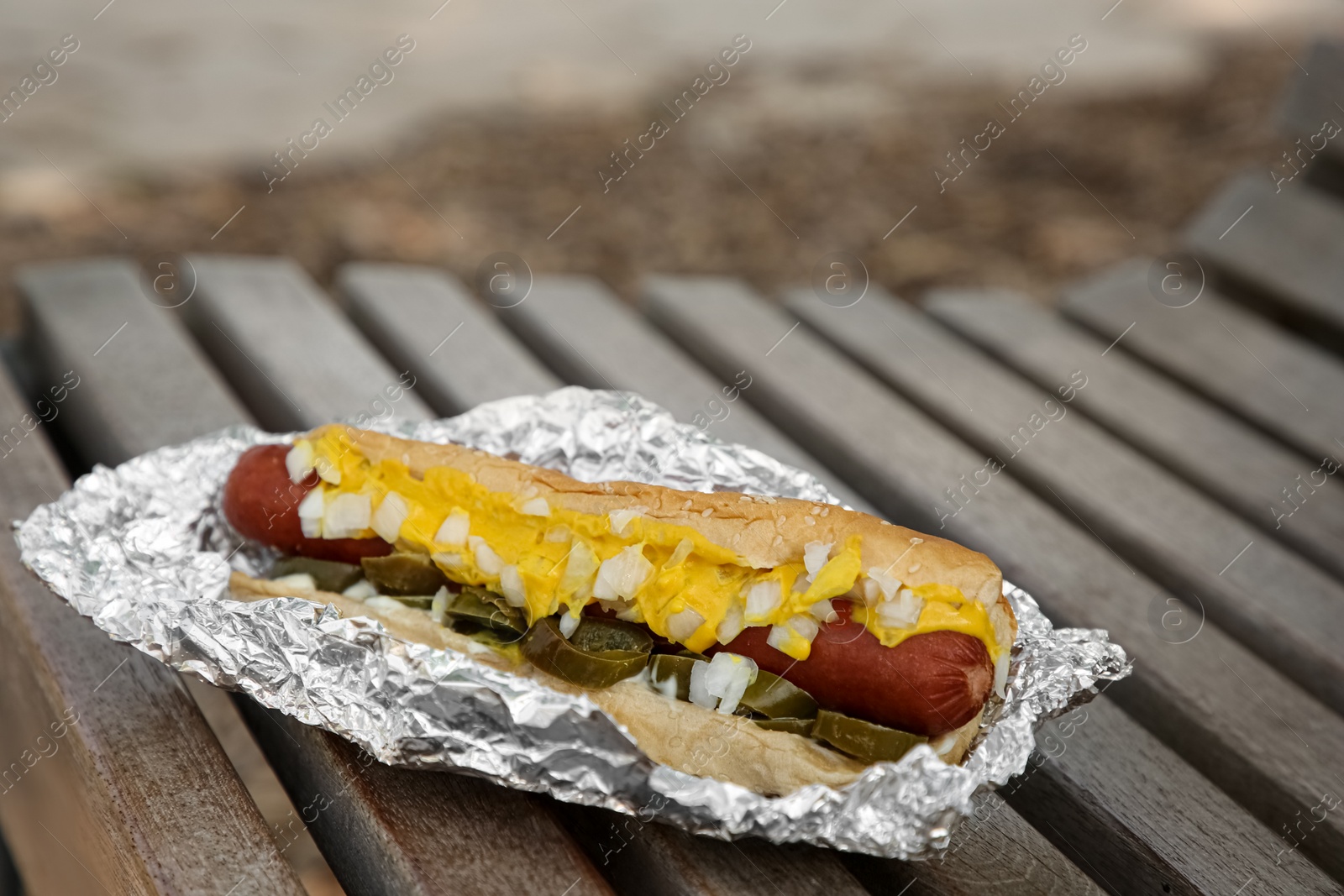 Photo of Fresh tasty hot dog with sauce on wooden surface outdoors