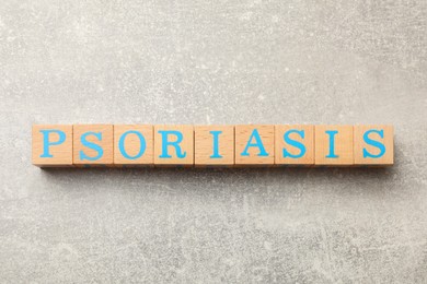 Photo of Word Psoriasis made of wooden cubes with letters on light gray textured table, top view