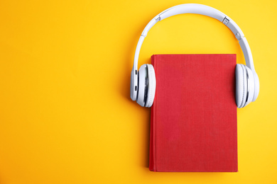 Photo of Book and modern headphones on yellow background, top view. Space for text