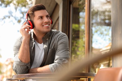 Photo of Handsome man with headphones listening to music in outdoor cafe, space for text