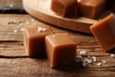 Yummy caramel candies and sea salt on wooden table, closeup