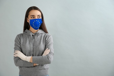 Image of Woman wearing medical mask with European Union flag on grey background, space for text. Coronavirus outbreak in Europe
