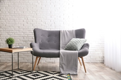 Comfortable sofa near brick wall in modern living room interior