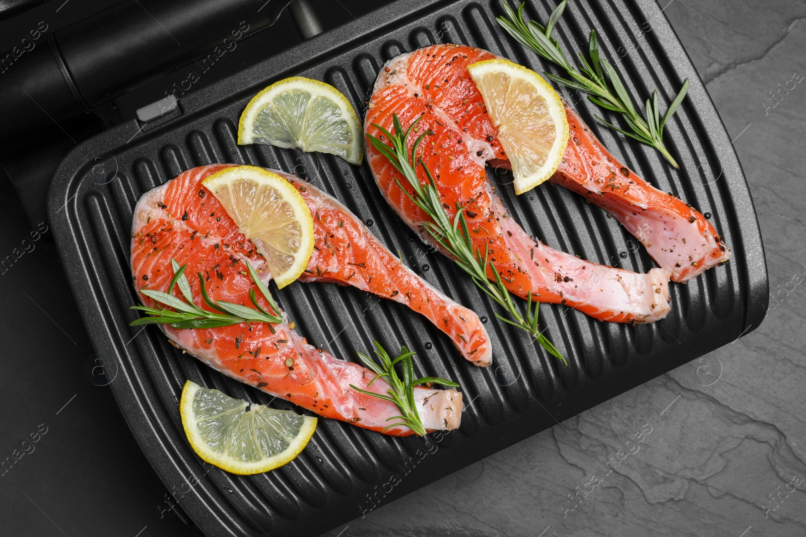 Photo of Cooking salmon. Grill with fresh fish steaks, lemon and rosemary on dark table, top view
