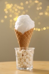 Photo of Sweet cotton candy in waffle cone on table against blurred lights