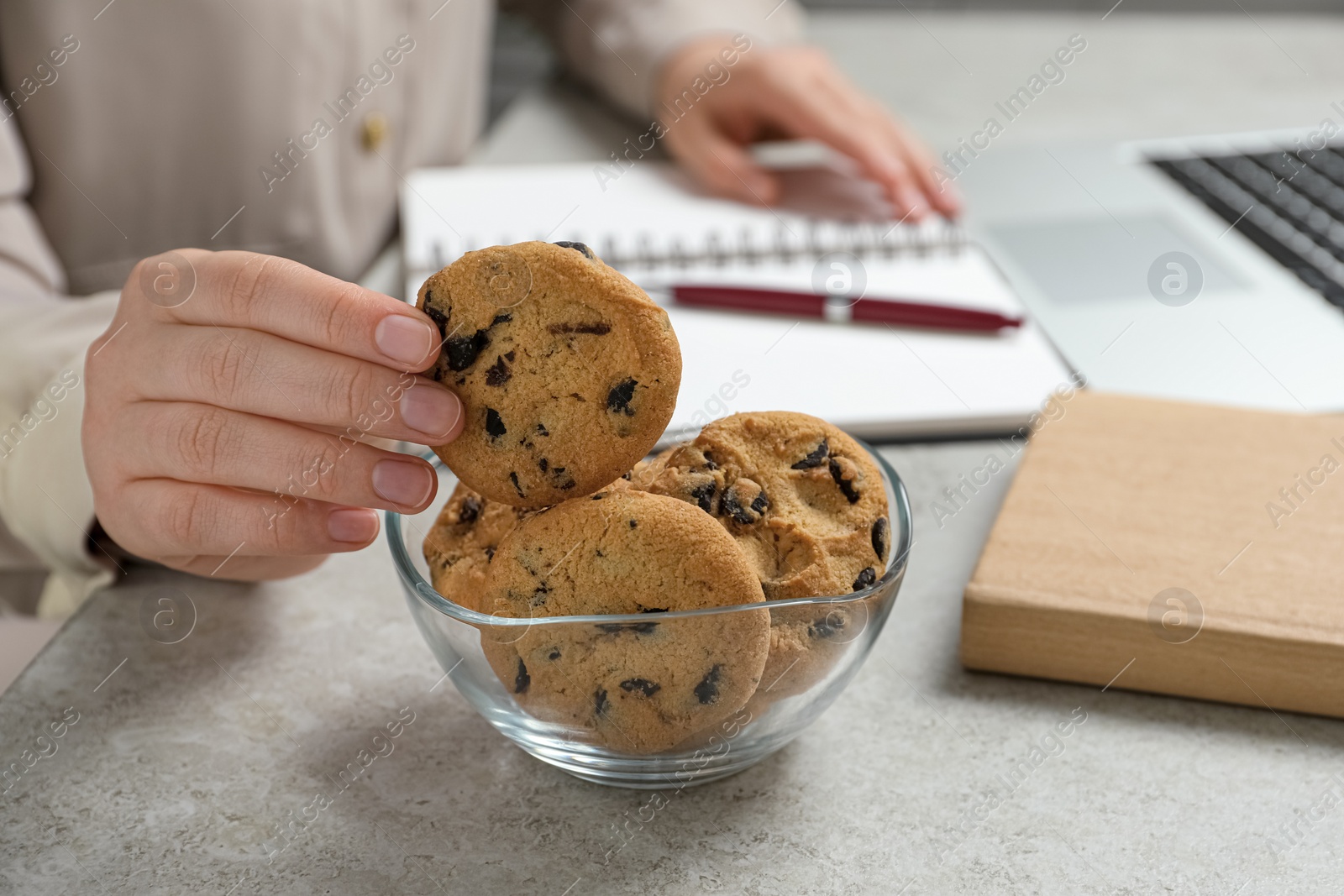 Photo of Office worker taking chocolate chip cookie from bowl at light gray table indoors, closeup