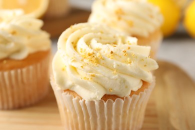 Photo of Tasty cupcakes with cream and lemon zest on wooden board, closeup