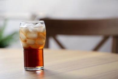 Glass of cola with ice on table against blurred background, space for text