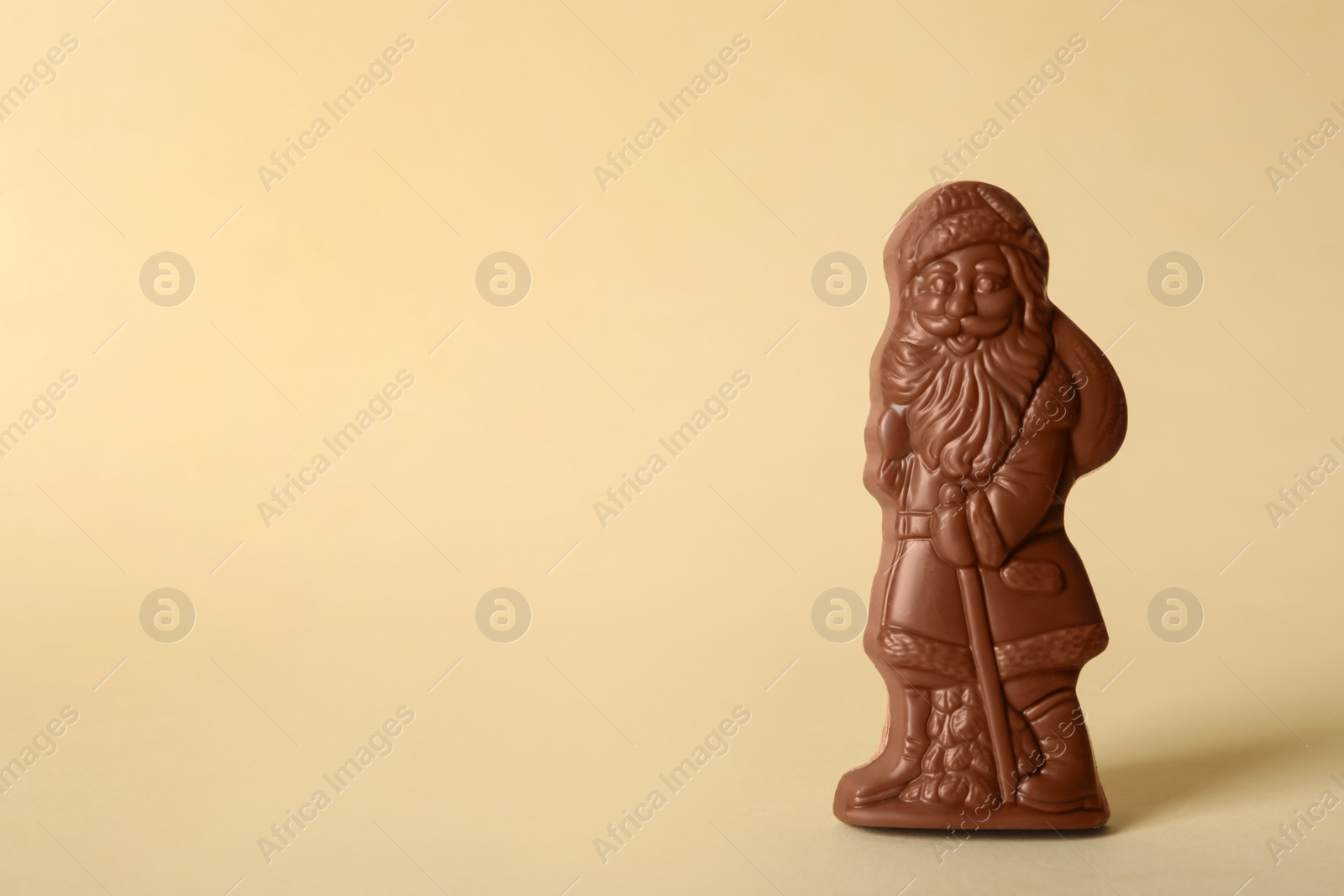 Photo of Sweet chocolate Santa Claus candy on beige background, space for text