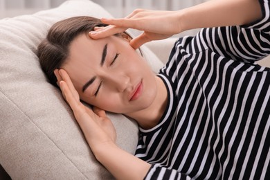 Photo of Sad woman suffering from headache on pillow indoors