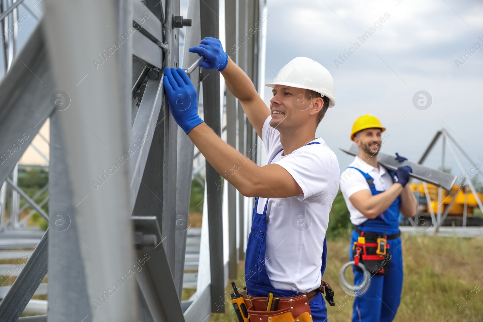 Photo of Workers building high voltage tower construction outdoors. Installation of electrical substation