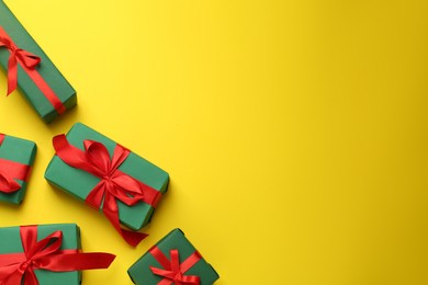 Photo of Many green gift boxes with red bows on yellow background, flat lay. Space for text