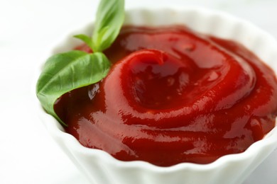 Bowl of tasty ketchup and basil on white table, closeup