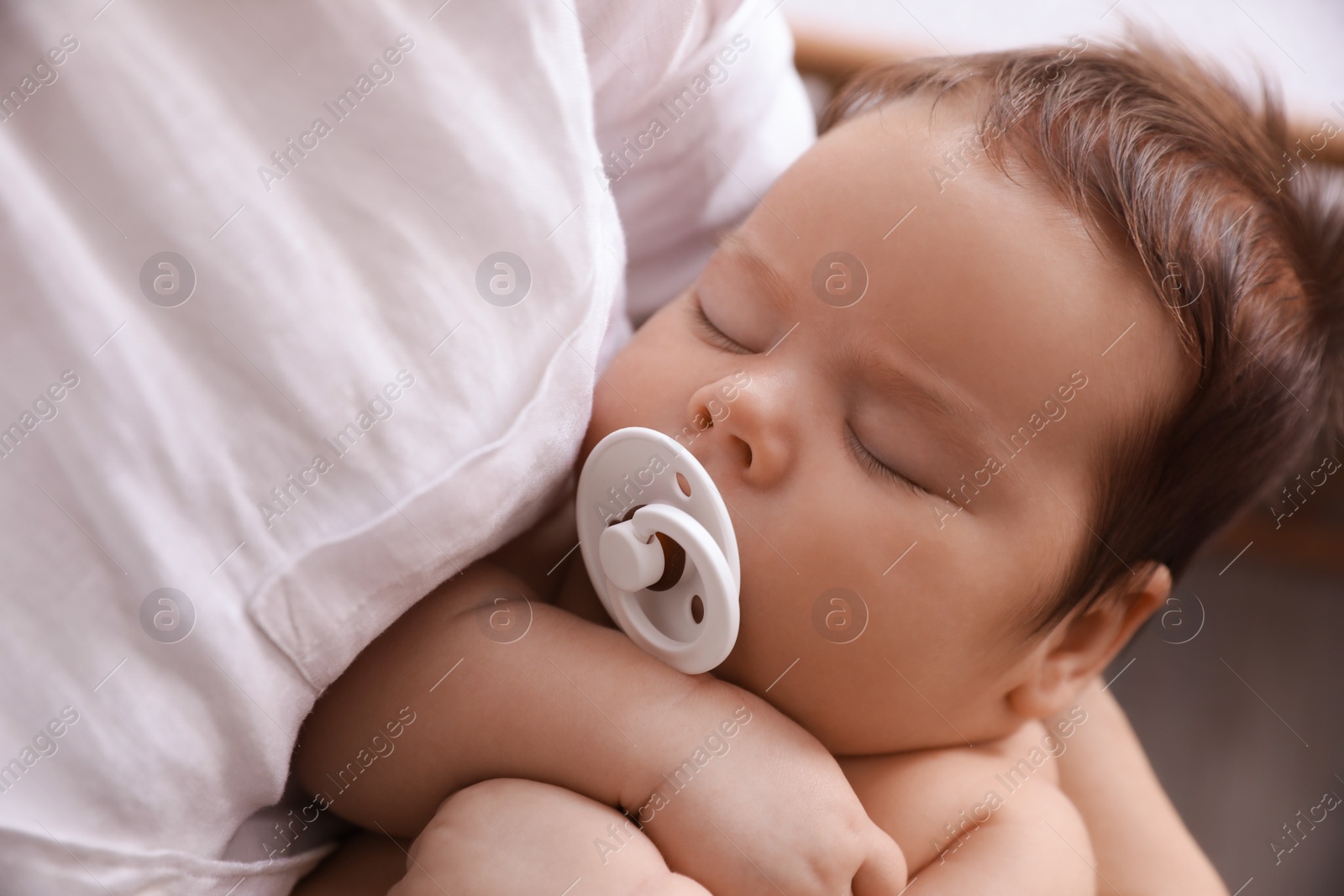 Photo of Mother holding her cute sleeping baby with pacifier on blurred background, closeup