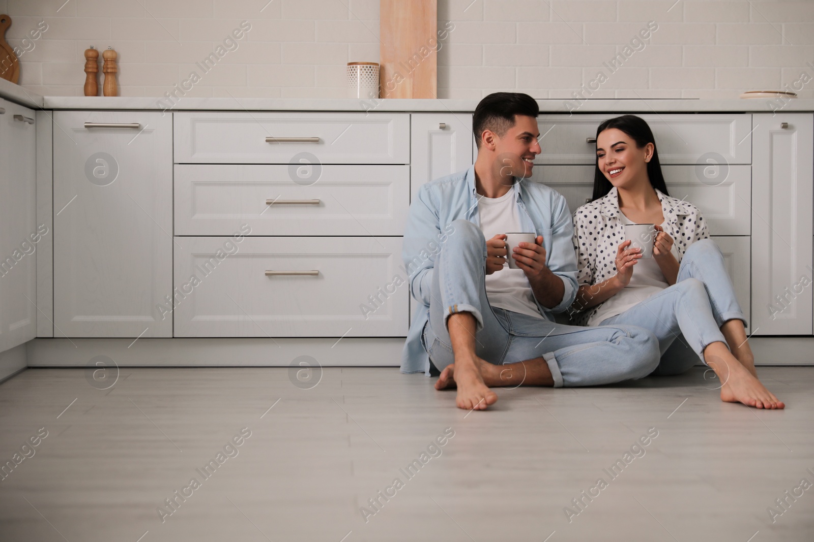 Photo of Happy couple sitting on warm floor in kitchen. Heating system