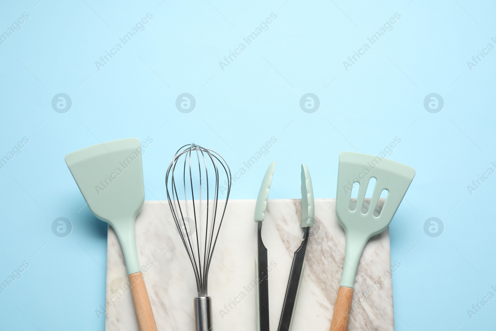 Photo of Different spatulas, whisk and tongs on light blue background, flat lay. Space for text