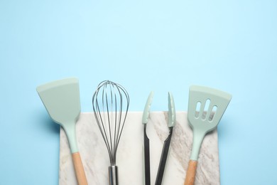 Different spatulas, whisk and tongs on light blue background, flat lay. Space for text