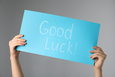 Photo of Woman holding blue card with words GOOD LUCK on light grey background, closeup