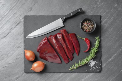 Photo of Cut raw beef liver with rosemary, onions, chili pepper, spices and knife on black table, top view