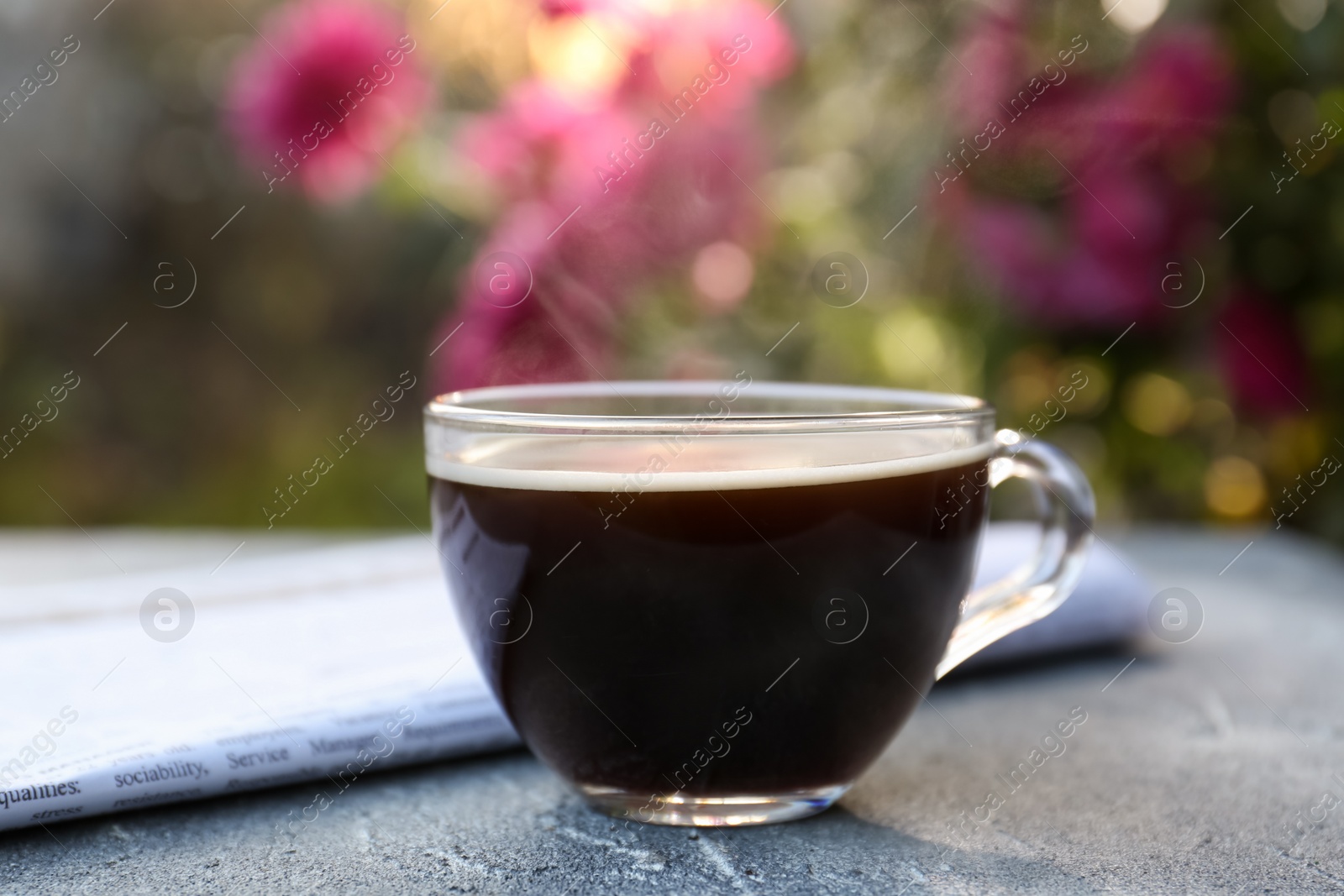 Photo of Glass cup with coffee and newspaper on grey table outdoors, closeup. Morning ritual