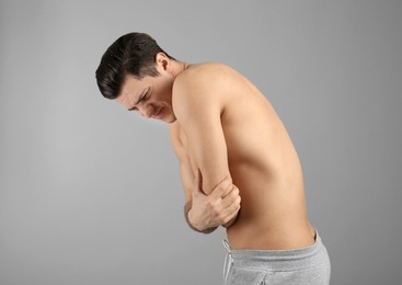 Young man suffering from pain in elbow on grey background