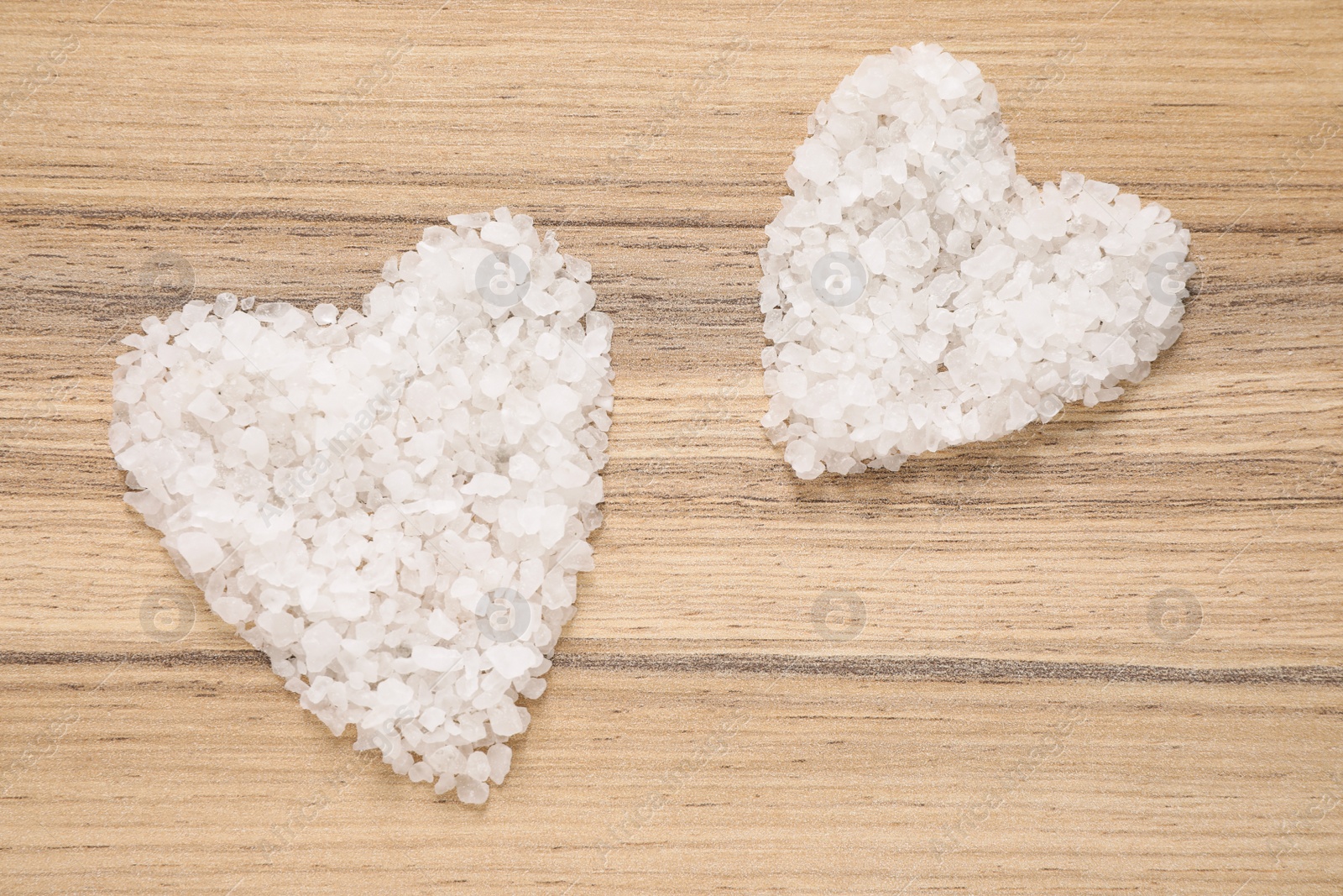 Photo of Heart shaped piles of sea salt for spa scrubbing procedure on wooden background, flat lay