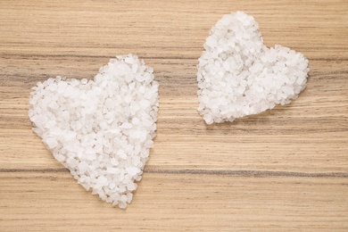 Heart shaped piles of sea salt for spa scrubbing procedure on wooden background, flat lay