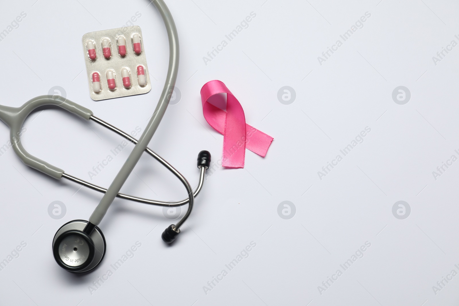 Photo of Breast cancer awareness. Pink ribbon, stethoscope and pills on white background, flat lay. Space for text