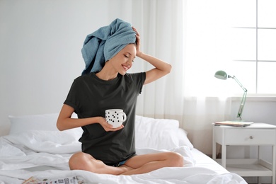Photo of Young happy woman with aromatic coffee on bed at home. Lazy morning
