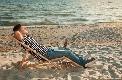 Photo of Man with laptop relaxing in deck chair on beach