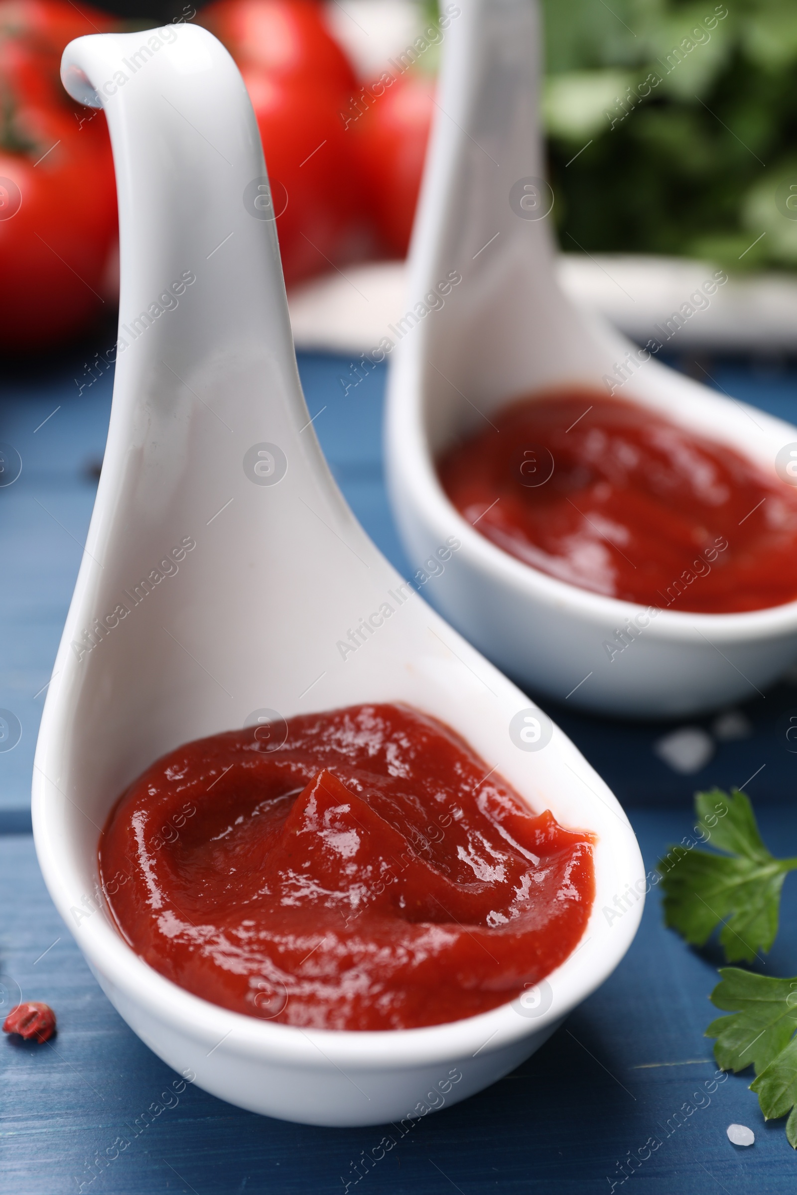 Photo of Organic ketchup in spoons on blue wooden table, closeup. Tomato sauce