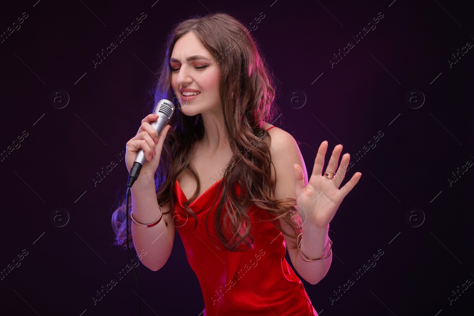 Photo of Emotional woman with microphone singing in color light on black background