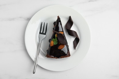 Photo of Piece of tasty homemade chocolate cake with mint and almonds on white marble table, top view