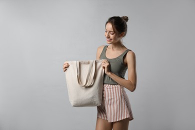 Happy young woman with blank eco friendly bag on light background