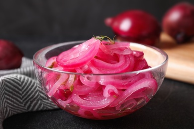 Bowl with tasty pickled onions on black table, closeup