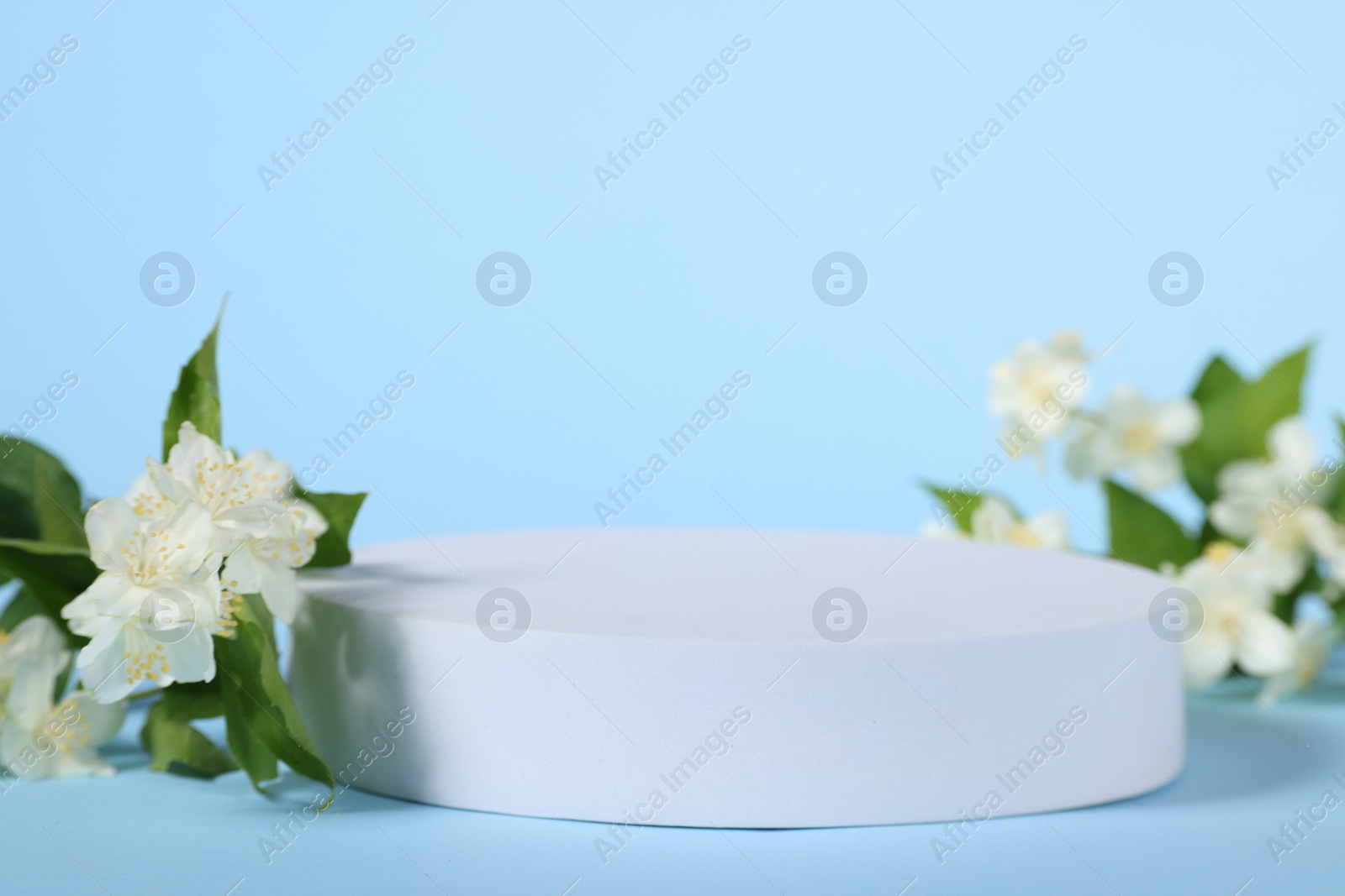 Photo of Presentation of product. White podium and beautiful jasmine flowers on light blue background, closeup. Space for text