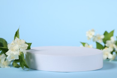 Presentation of product. White podium and beautiful jasmine flowers on light blue background, closeup. Space for text