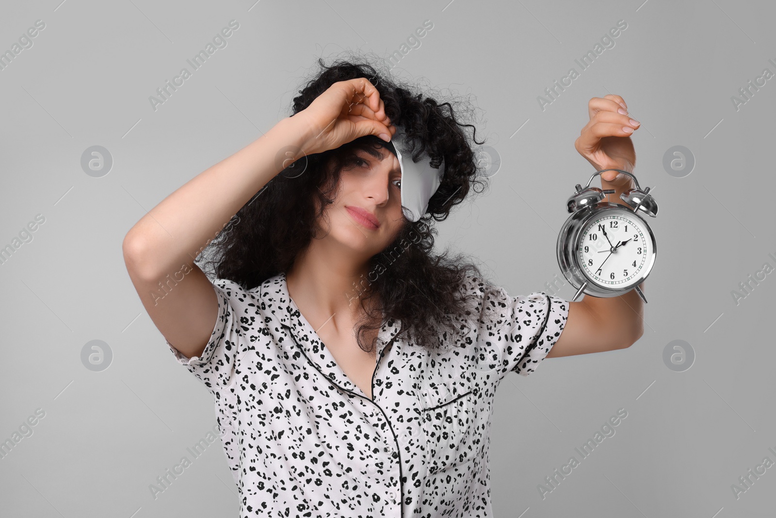 Photo of Tired young woman with sleep mask and alarm clock on light grey background. Insomnia problem