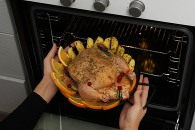 Photo of Woman putting chicken with orange and potato slices into oven, closeup