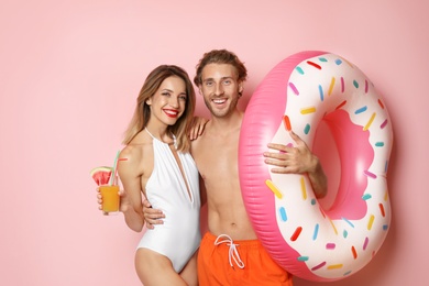 Photo of Happy young couple in beachwear with inflatable ring and cocktail on color background