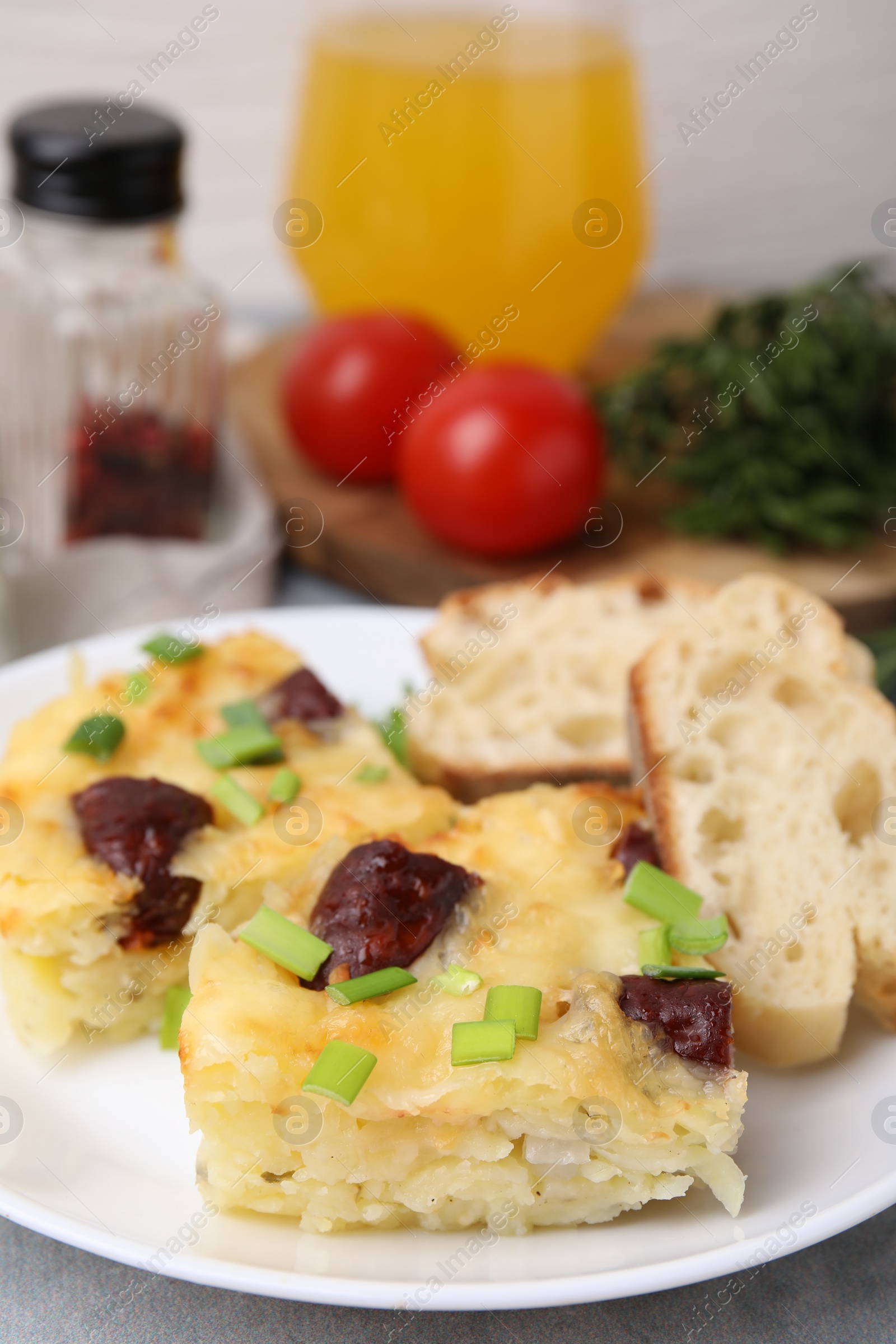 Photo of Tasty sausage casserole with green onion and bread on grey table, closeup