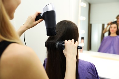 Photo of Stylist drying client's hair in beauty salon, closeup