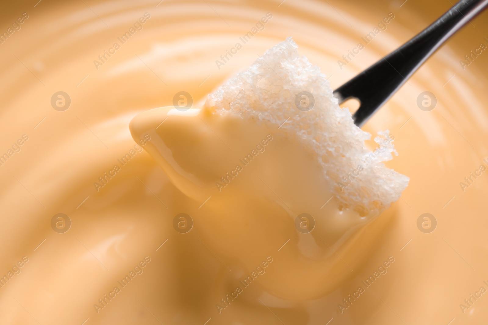 Photo of Dipping bread into tasty cheese fondue, closeup