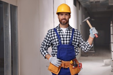 Photo of Professional builder in uniform with hammer and tool belt indoors