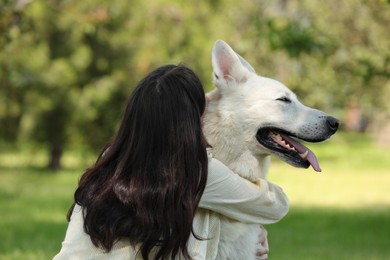 Young woman hugging her white Swiss Shepherd dog in park, back view