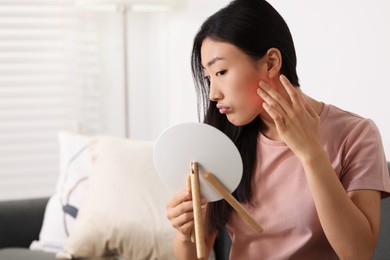 Photo of Suffering from allergy. Young woman with mirror checking her face in living room