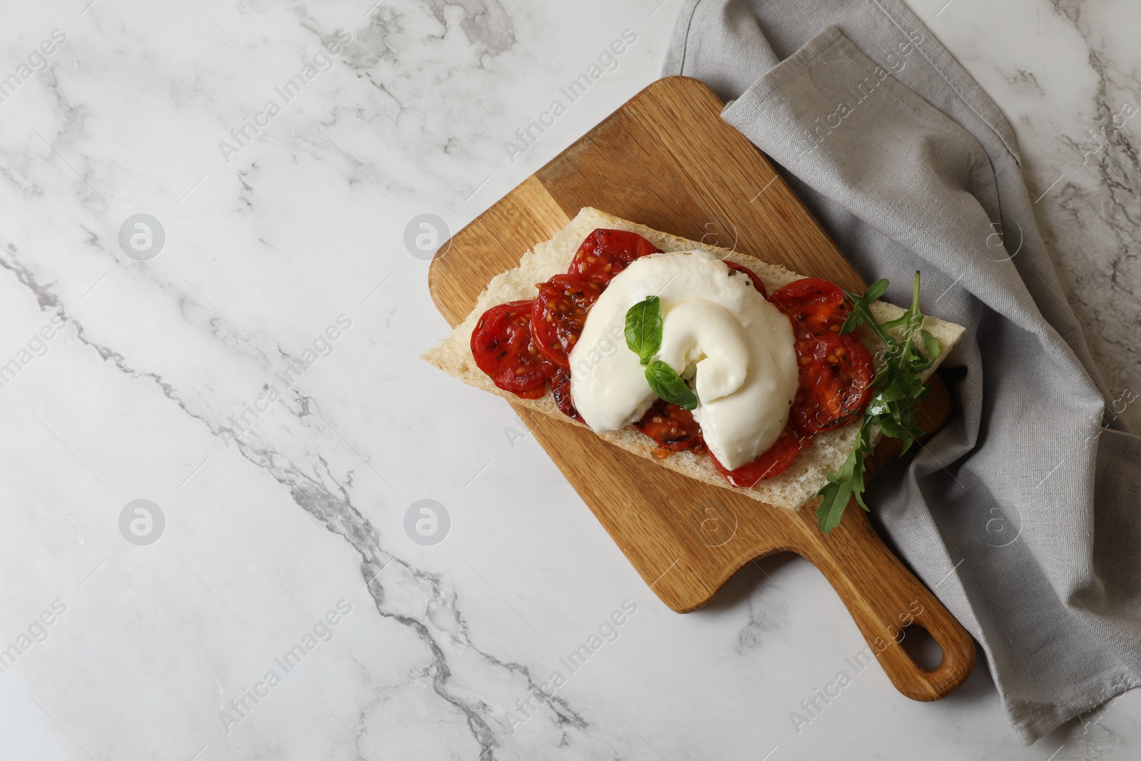 Photo of Toast with delicious burrata cheese, tomatoes and arugula on white marble table, top view. Space for text